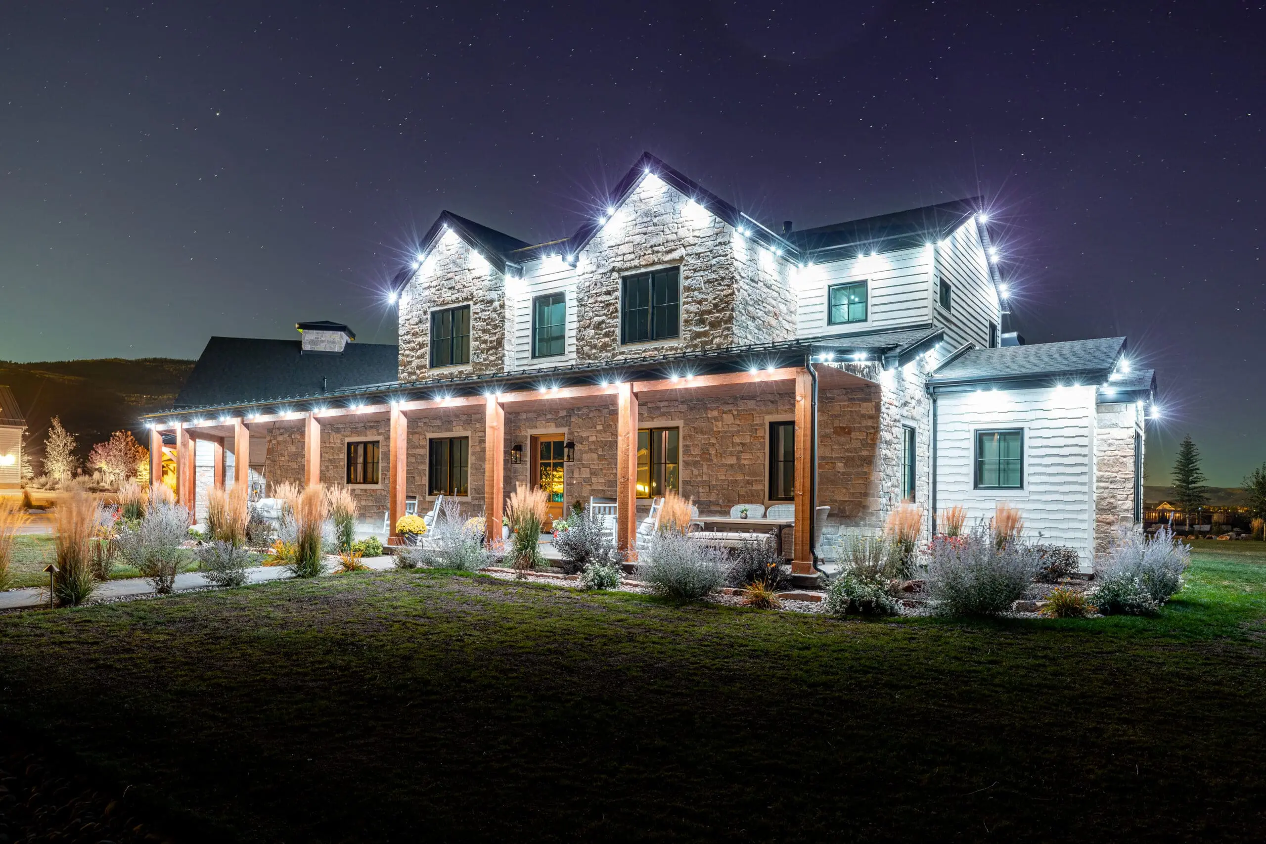 Two-story stone and siding home at night with white permanent lights along every roofline